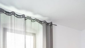 A modern living room with a grey sofa, two pillows, a window with sheer curtains, and a lamp on a side table. - Modern Apartment - Main Square - 30 m² - Comfort (Leoben)