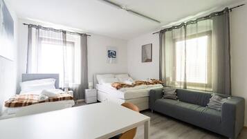 A compact hotel room with a bed, a sofa, a small table, and a window with curtains.