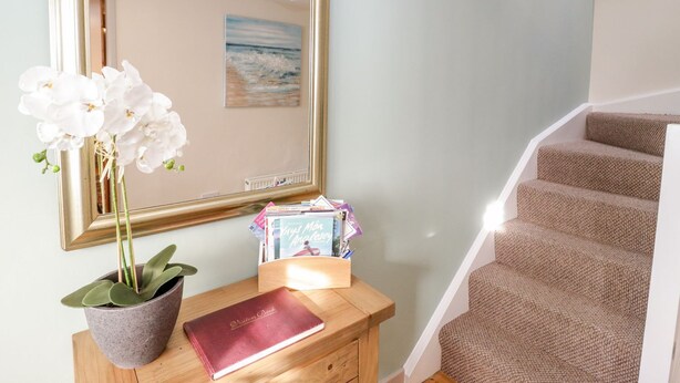 A staircase with carpeted steps, a wooden desk with a book and a potted plant, and a large mirror reflecting a painting. - Eryri View Retreat (Beaumaris)