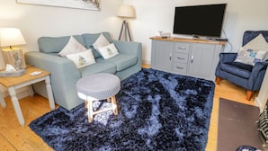 A living room with a sofa, a TV, a lamp, a small round table, and a blue rug. - Eryri View Retreat (Beaumaris)