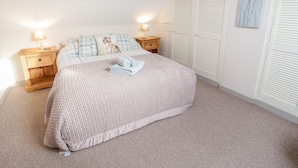 A bedroom with a bed, two bedside tables, a nightstand, a wall-mounted artwork, and a set of white louvered closets. - Eryri View Retreat (Beaumaris)