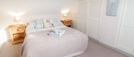 A bedroom with a bed, two bedside tables, a nightstand, a wall-mounted artwork, and a set of white louvered closets.