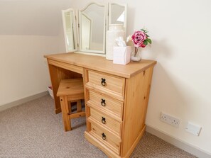 A wooden dresser with drawers and a mirror, a small stool, and a vase with a flower. - Eryri View Retreat (Beaumaris)