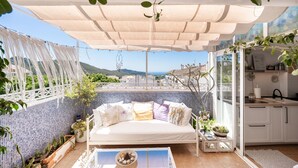 Zona d'estar exterior acollidora amb un sofà blanc, plantes en testos i una taula de vidre.