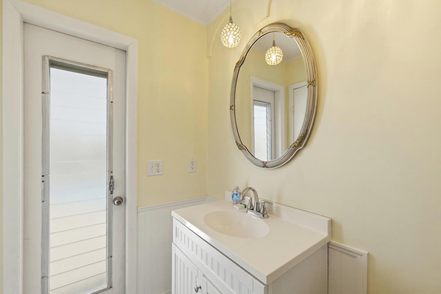 A bathroom with a white vanity, a round mirror with a gold frame, and two pendant lights.