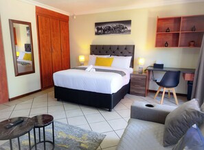 Une chambre d’hôtel comprenant un lit, des tables de chevet, un bureau, une chaise, un canapé, un miroir et un tableau accroché au mur.