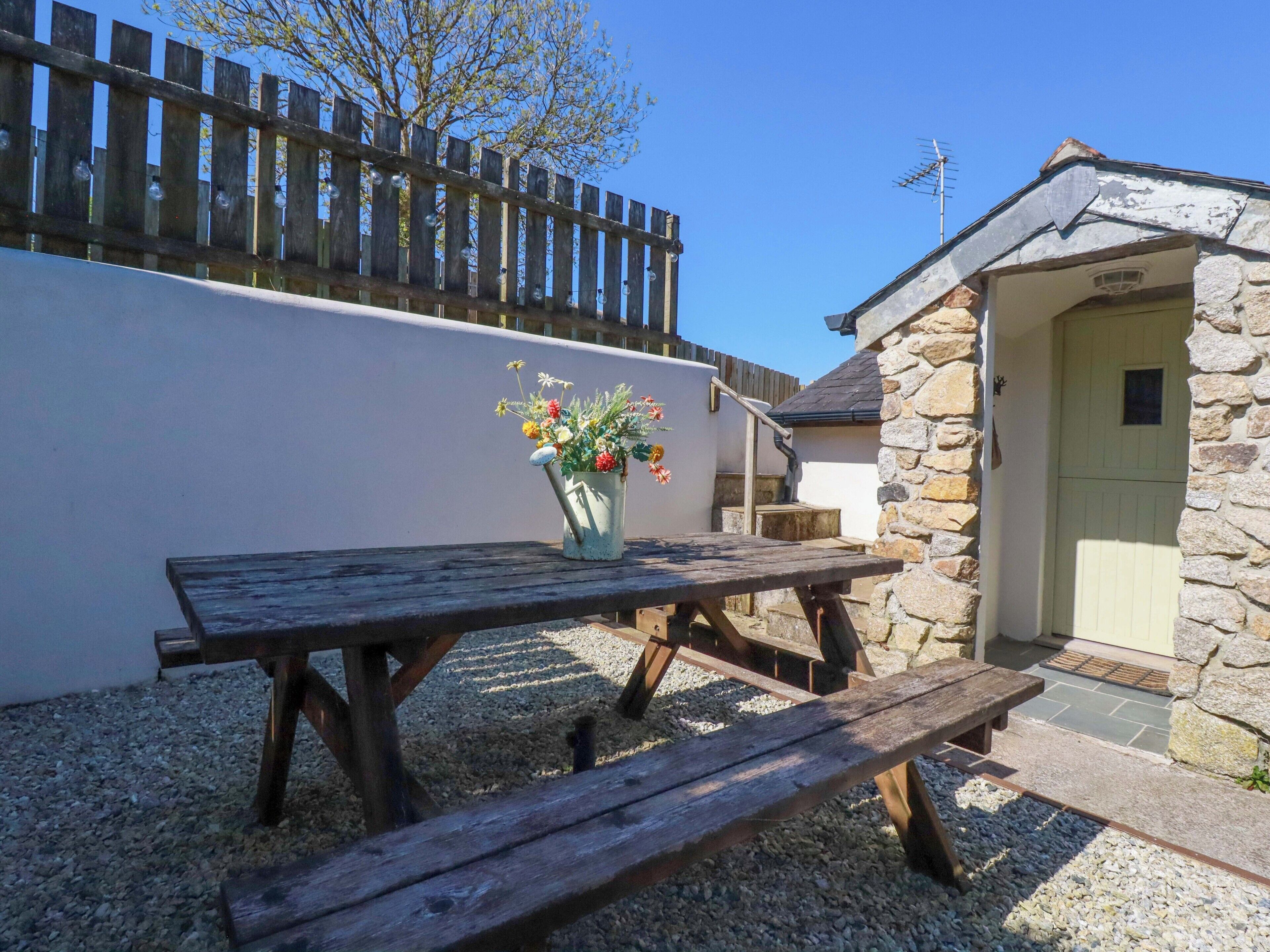 A wooden picnic table with a flower pot, a stone building with a door, and a wooden fence.