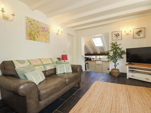 A living room with a brown leather sofa, a flat-screen TV, and a kitchen in the background. - Millies Place (St Austell)