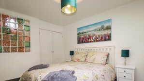 A bedroom with a bed, nightstands, a painting, a wardrobe, and a decorative window. - Millies Place (St Austell)
