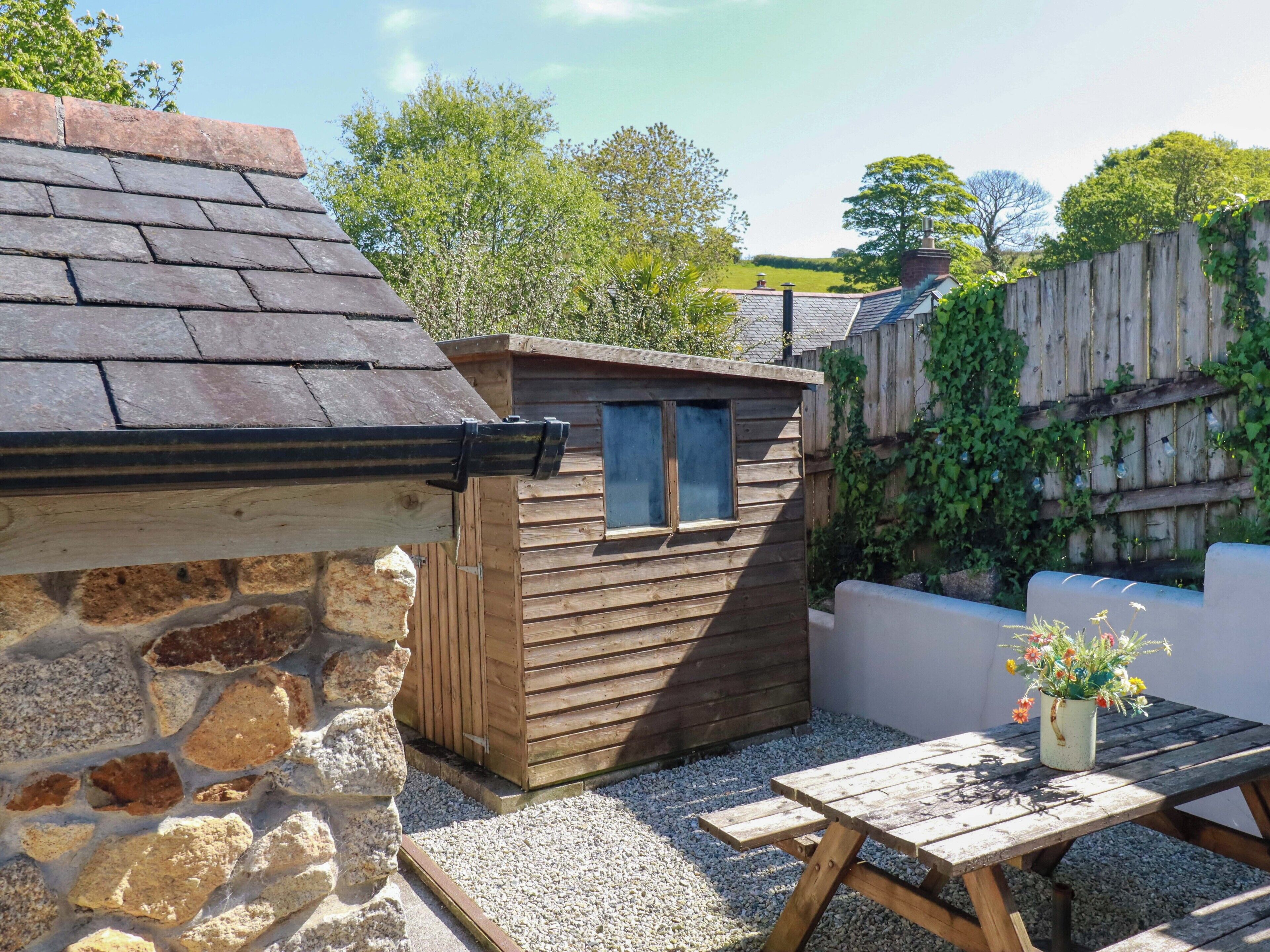 A stone wall, wooden shed, wooden fence, and a wooden table with a flower pot.