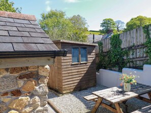 A stone wall, wooden shed, wooden fence, and a wooden table with a flower pot. - Millies Place (St Austell)
