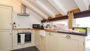 A kitchen with white cabinets, a microwave, a kettle, and a window with a view. - Millies Place (St Austell)