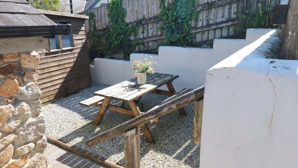 A wooden picnic table with a flower pot, surrounded by gravel and a stone wall. - Millies Place (St Austell)