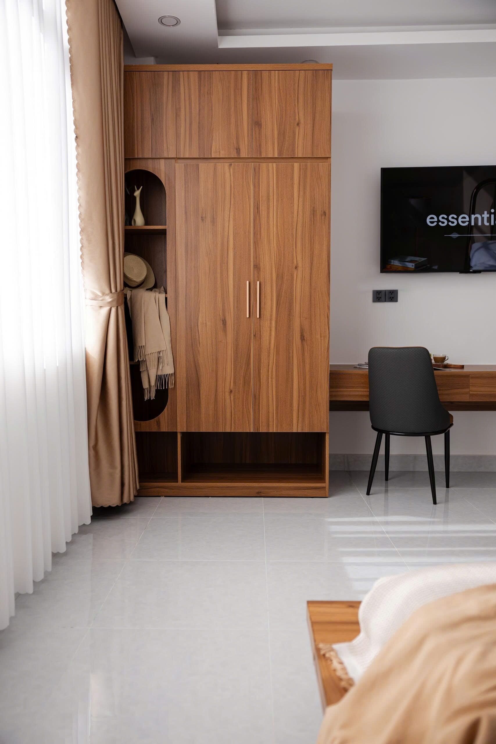 A modern bedroom with a wooden wardrobe, a desk, a chair, and a television.