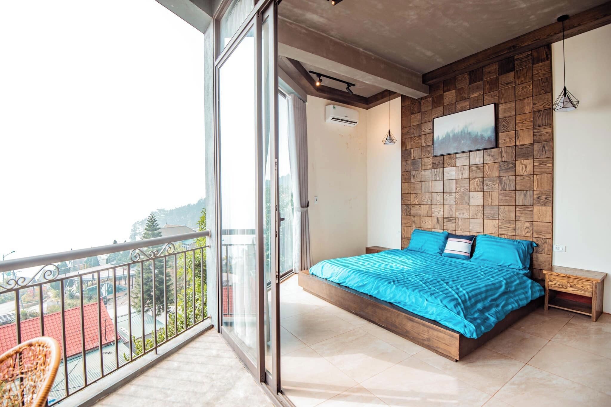 Un dormitorio con una cama grande, cabecera de madera, balcón con una silla y vistas a la ciudad.