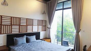 A bedroom with a bed, a nightstand, a window with curtains, and a view of greenery outside.
