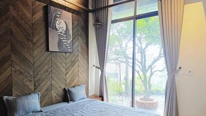 A bedroom with a large bed, a herringbone-patterned wall, a hanging light, and a view of the outdoors.