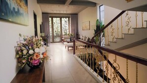 A hallway with a staircase, a floral arrangement, and a view through a glass door.