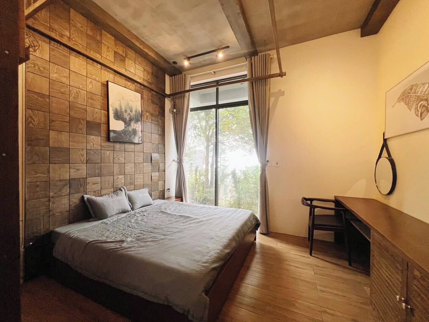 A bedroom with a bed, a desk, a window with curtains, and a painting on the wall.