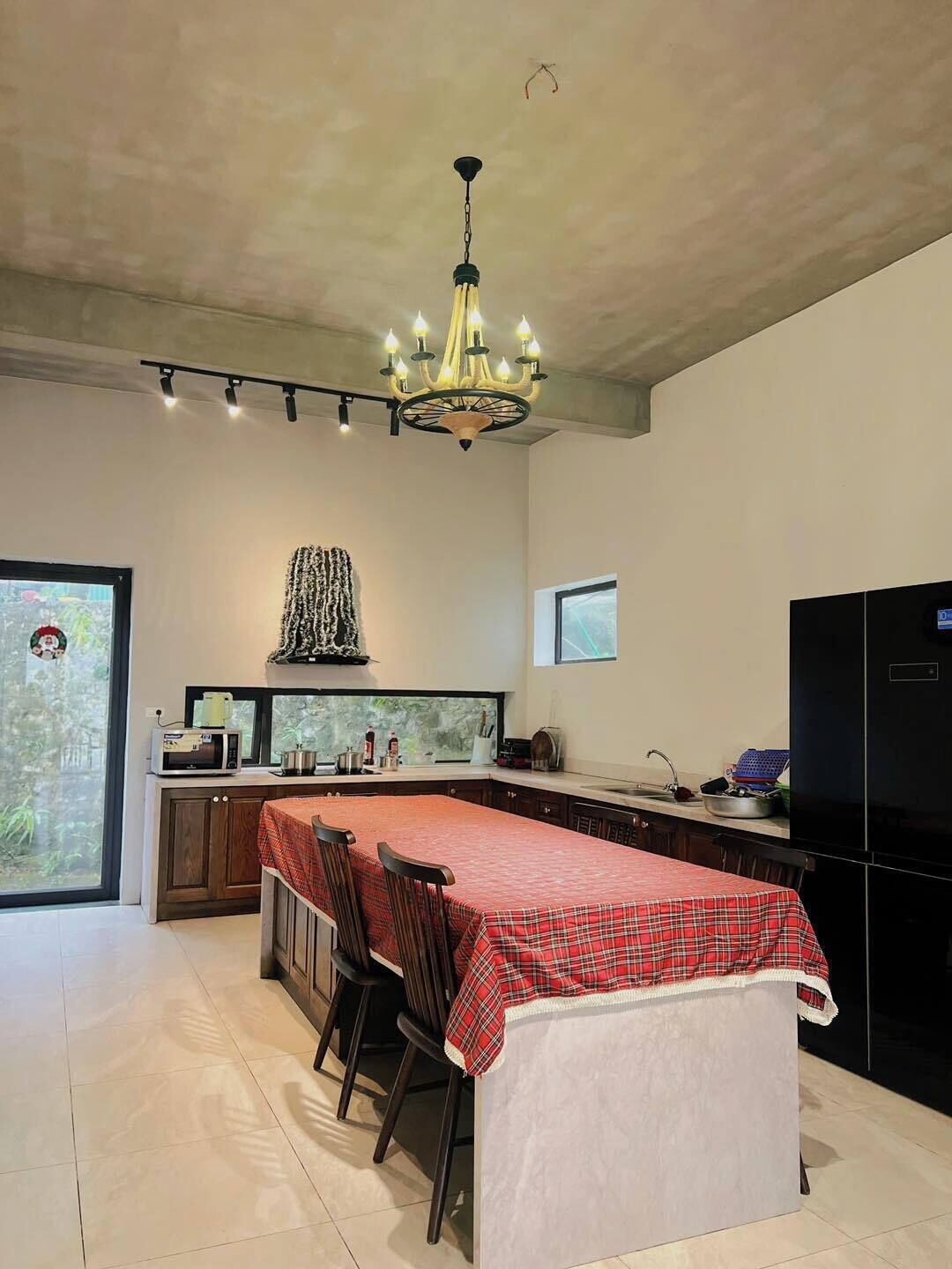 A modern kitchen with a dining area, a chandelier, and a view through a large window.