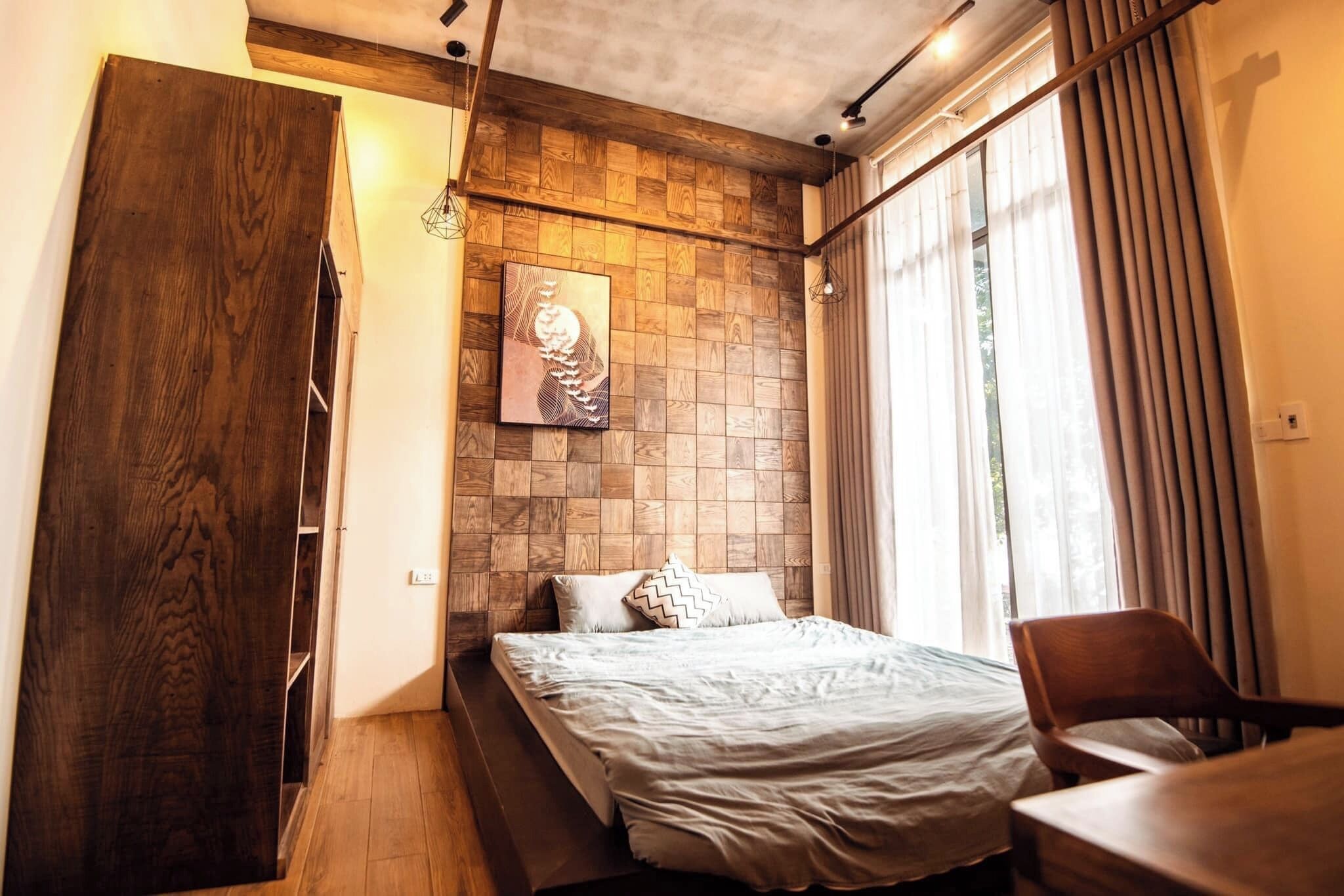 A bedroom with a bed, a wooden wardrobe, a painting on the wall, and a window with curtains.