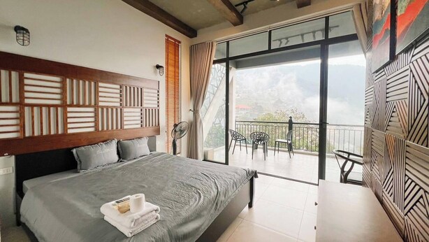 A bedroom with a large bed, a balcony with chairs, and a view of the landscape.