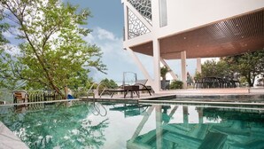 A clear swimming pool with lounge chairs and a modern building with a geometric facade.
