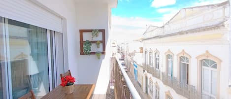 A balcony with a wooden table and chairs, a hanging plant, and a view of historic buildings.