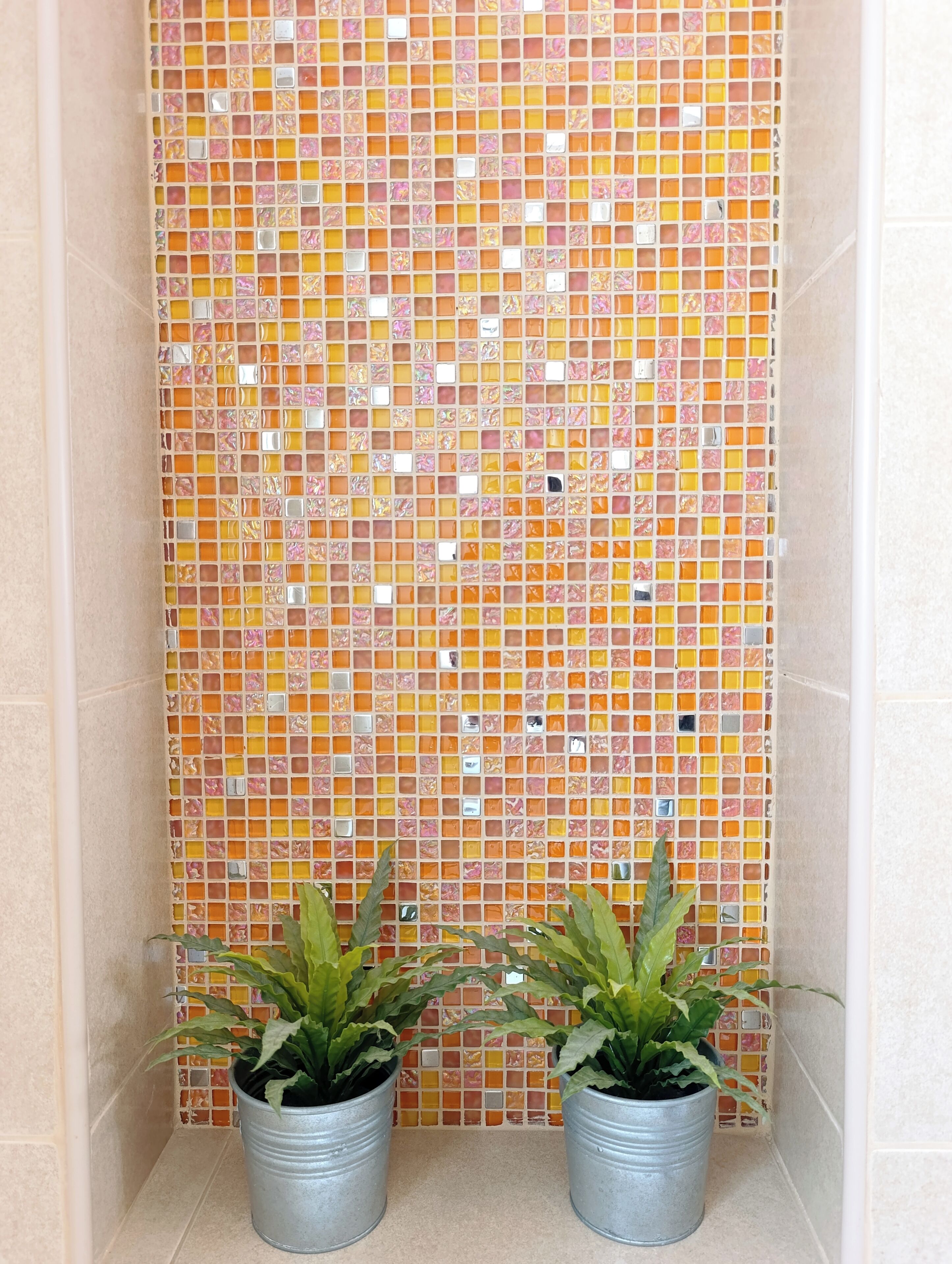 A tiled wall with a mosaic pattern, two potted plants, and a corner with beige tiles.