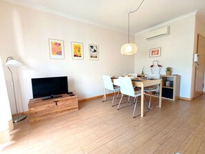 A modern living room with a TV, wooden storage unit, dining area with chairs, and artwork on the wall. - Apartment "Lavadeiras7" - Downtown Olhão (Olhão)