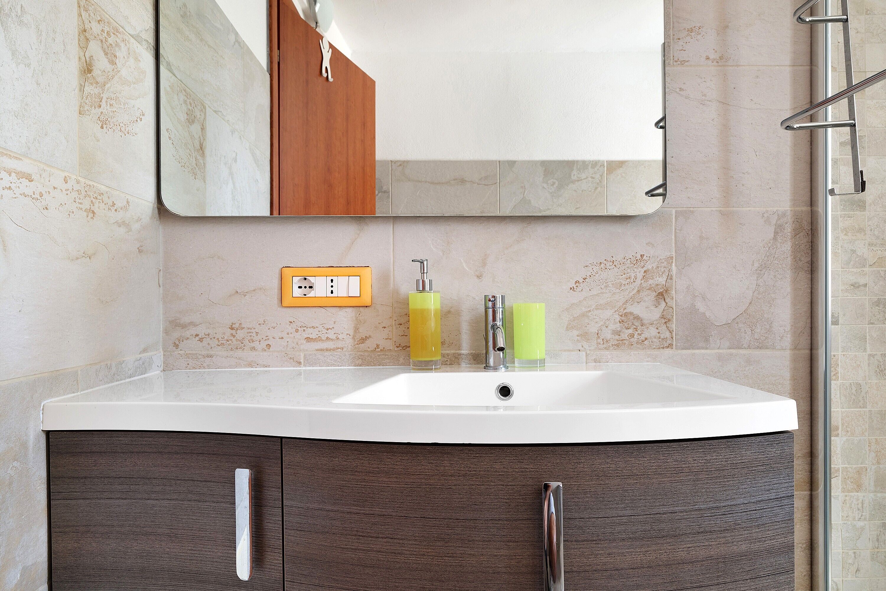 Une salle de bain avec un lavabo blanc, un miroir, un meuble en bois et un espace douche.