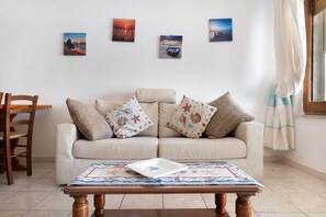 Ein Wohnzimmer mit einer Couch, einem Holztisch und einem Sessel. An der Wand hängen vier gerahmte Bilder.