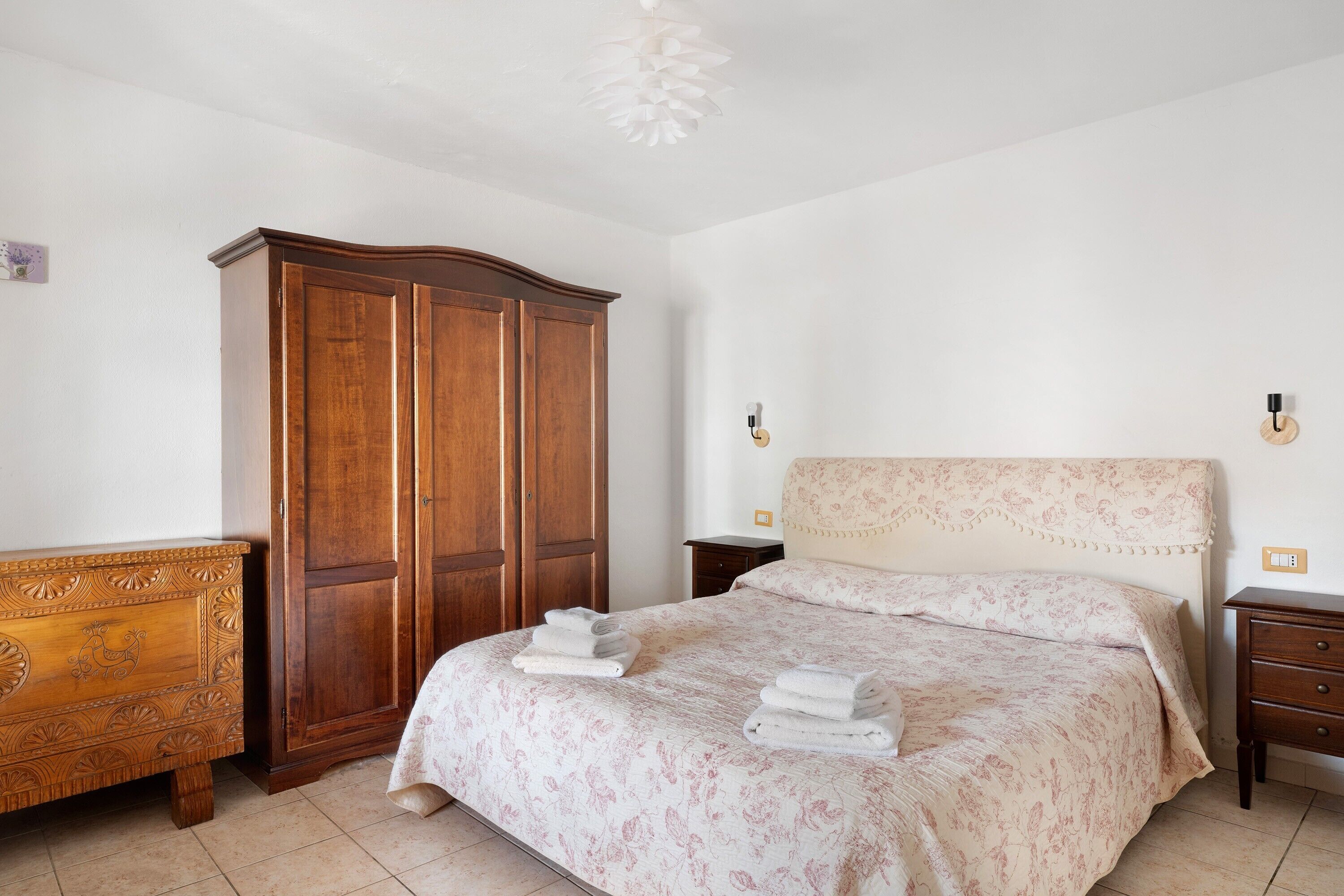 Ein Schlafzimmer mit einem Bett, einem Holzschrank, einem Nachttisch und einer Wandleuchte.