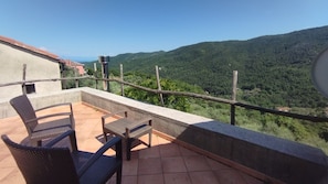 A balcony with wicker chairs and a table, overlooking a mountainous landscape.