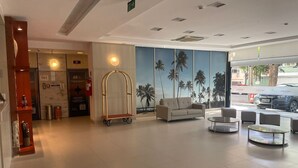 Eine Hotellobby mit einer Rezeption, einer Couch, einem Wagen und einem Wandbild von Palmen.