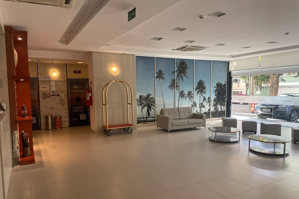 A hotel lobby with a reception desk, a sofa, a cart, and a mural of palm trees.