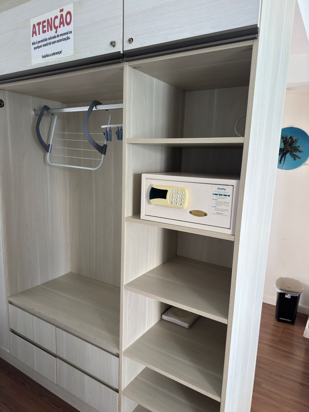 Quarto de hotel com minibar, pequena escrivaninha e telefone fixado na parede.