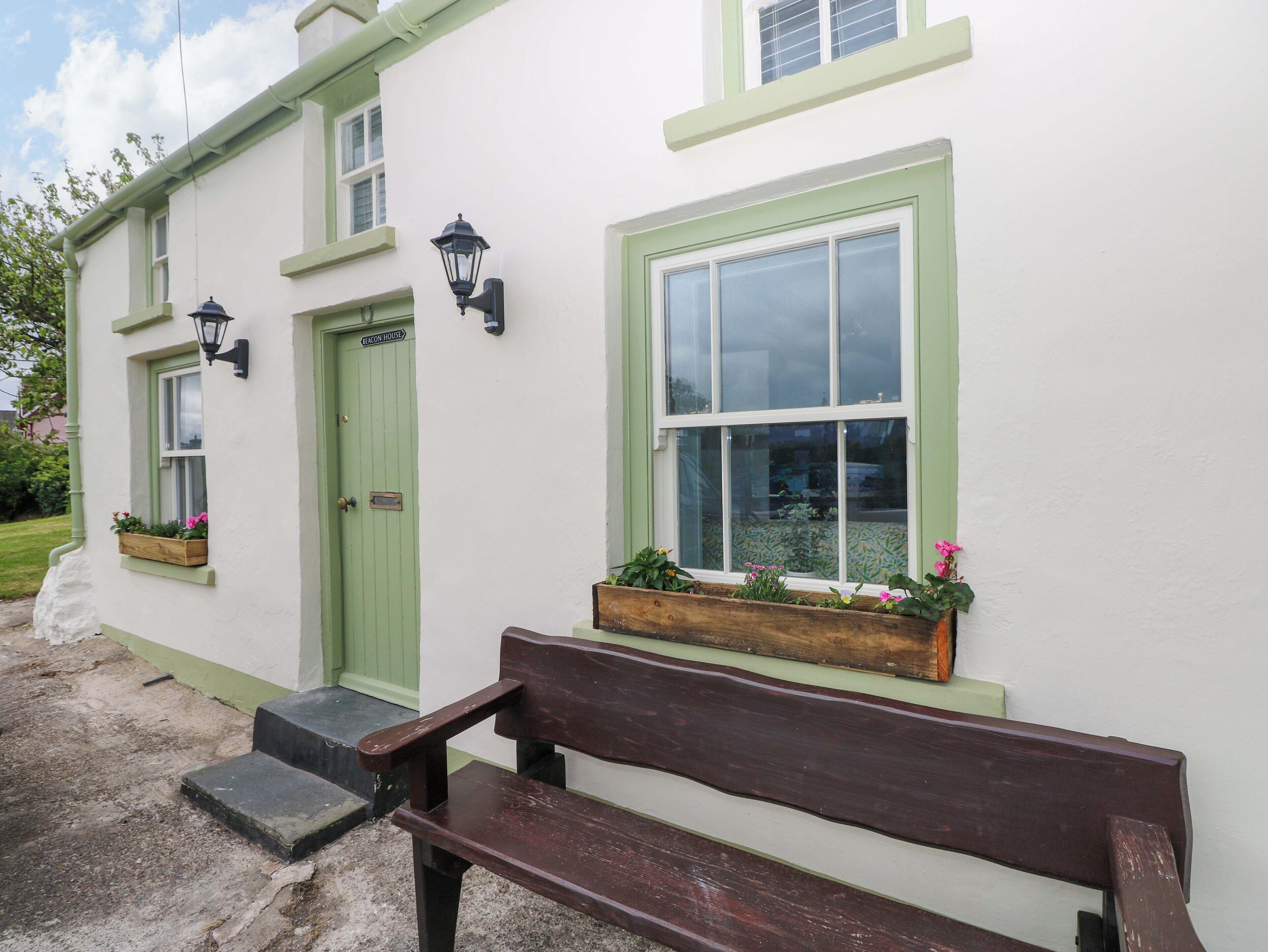 A white building with green trim, a bench, and flower boxes on the windowsills.