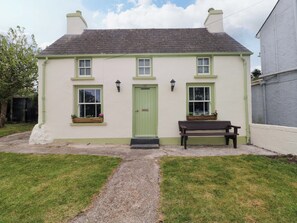 A two-story house with a green door, two windows with flower boxes, a bench outside, and a gravel path leading to the entrance. - Beacon House (Haverfordwest)