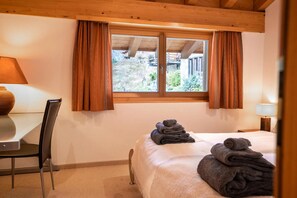 A hotel room with a bed, a chair, a table, and a window with curtains. - Luxury Alpine Duplex with Matterhorn Views & Sunny Panoramic Balcony (Zermatt)