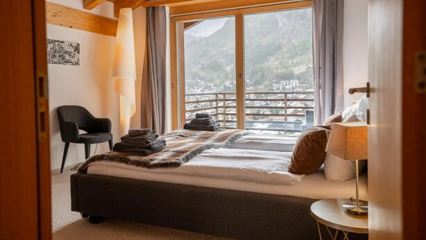 Une chambre à coucher avec un lit, une chaise, une lampe et une vue sur un paysage montagneux.