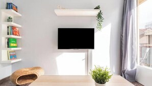 Een kamer met een wandgemonteerde flatscreen-tv, een houten tafel, een geweven dierenbed en een potplant.