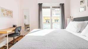 Een hotelkamer met een bed, een bureau, een stoel, een raam met gordijnen en uitzicht op gebouwen.
