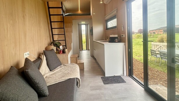A modern interior with a sofa, a kitchen, and a view through large glass doors. - Tiny House by Gad Bourgeois "La parenthèse nature" 8km from Pairi Daiza (Chièvres)