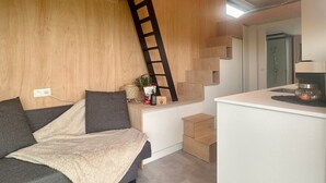 A modern living space with a sofa, a small kitchen area, and a staircase. - Tiny House by Gad Bourgeois "La parenthèse nature" 8km from Pairi Daiza (Chièvres)