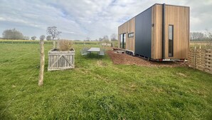 A modern wooden building with a flat roof, a large sliding door, and a small attached structure with a table and chairs. - Tiny House by Gad Bourgeois "La parenthèse nature" 8km from Pairi Daiza (Chièvres)