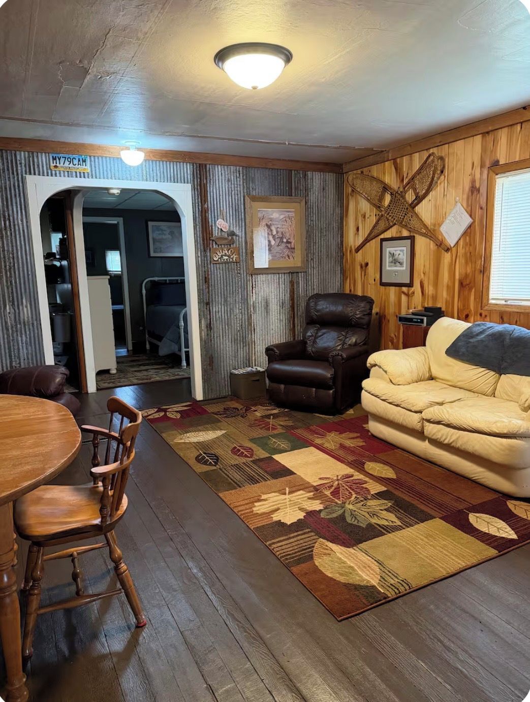 Una sala de estar acogedora con piso de madera, un sillón de cuero, un sofá, una mesa de comedor con sillas y una alfombra estampada.
