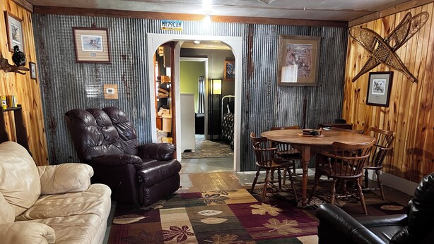 A room with a leather sofa, a dining table with chairs, a patterned rug, and framed pictures on the walls.