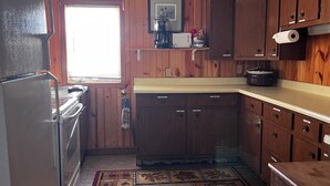 A kitchen with wooden cabinets, a refrigerator, a stove, a window, and a patterned rug.