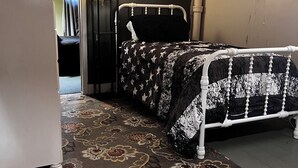 A bedroom with a bed, a nightstand, a dresser, a patterned rug, and a wooden ceiling.
